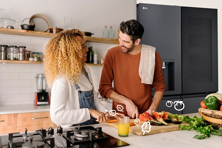 La pareja sonriente cocina delante del frigorífico.