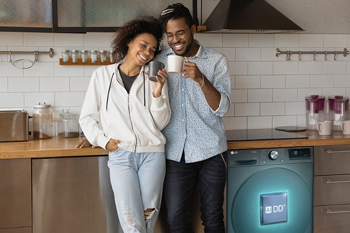 La pareja que sostiene la copa está de pie al lado de la lavadora. Una línea de inteligencia artificial sale de la lavadora con el logotipo AIDD sobre ella y detecta sus prendas.