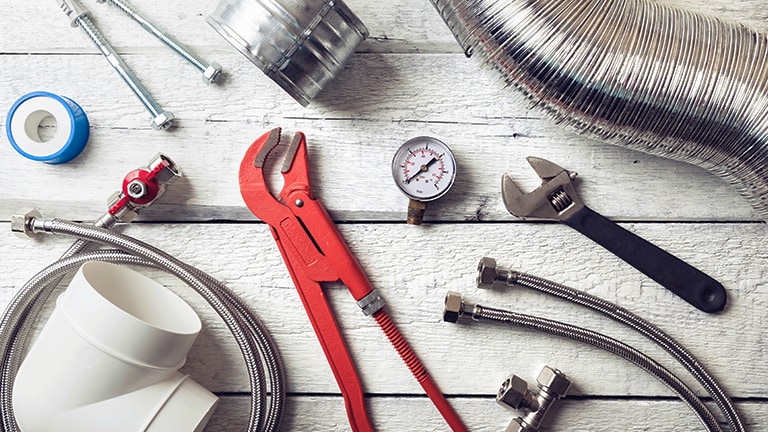 On a white wooden floor, a variety of tools and supplies are arranged, with a red monkey wrench taking center stage.
