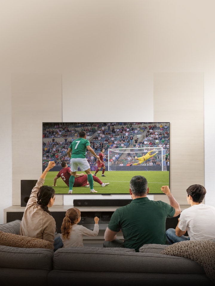Una familia sentada en el sofá de la sala disfruta y celebra un partido de fútbol en una pantalla grande.
