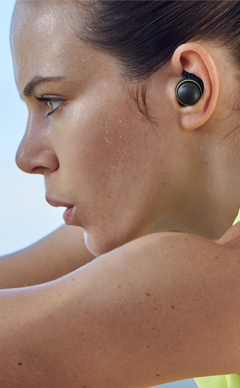 Une femme transpire en faisant de l’exercice avec des écouteurs TONE Free fit.