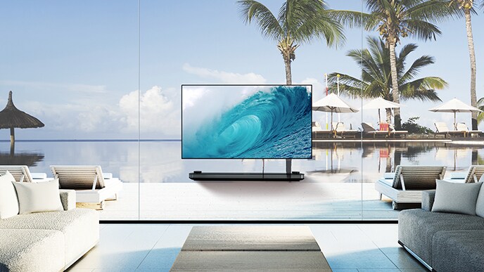 LG SIGNATURE OLED TV W montre la vague fraîche sur son écran tout en étant posé dans le salon avec la vue sur l'océan bleu au-delà de la fenêtre.
