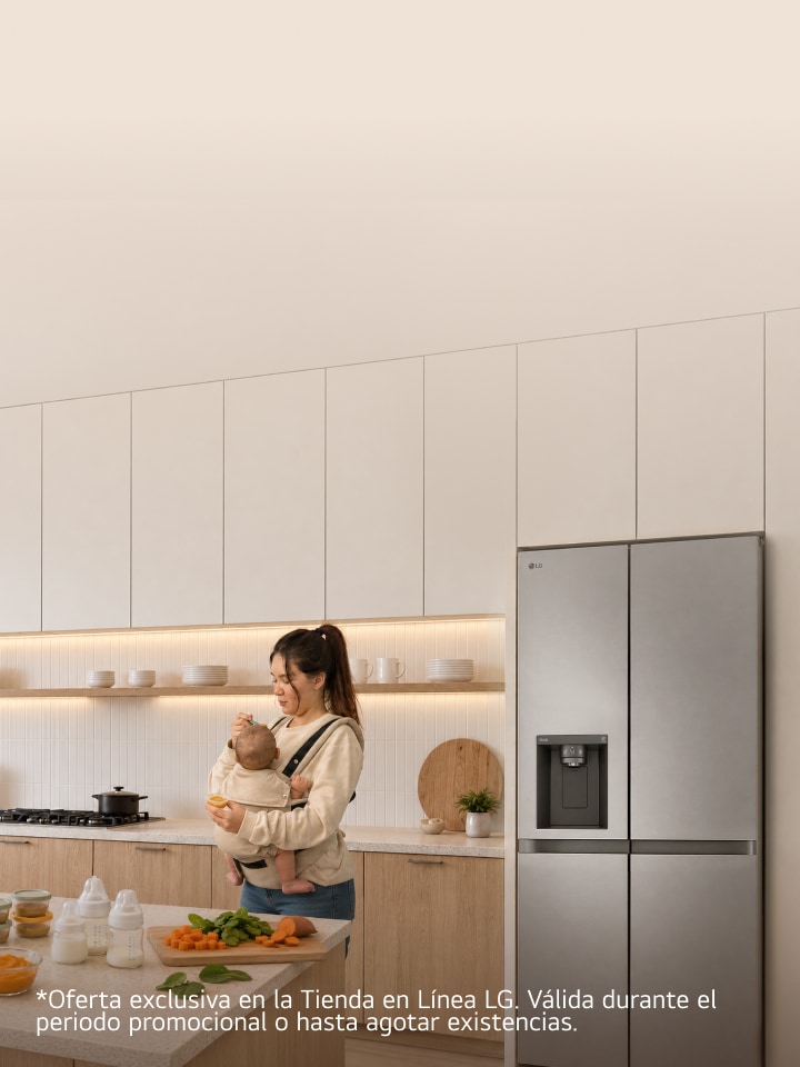 Una madre con su bebé en un portabebés prepara alimentos en una cocina moderna junto a un refrigerador LG de acero inoxidable.