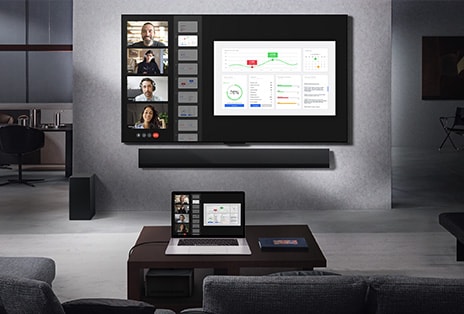Widok salonu z perspektywy kanapy na LG True Wireless TV i LG Soundbar. Na stoliku leży laptop połączony z modułem Zero Connect Box pod stolikiem. Obraz z wideorozmowy z laptopa jest wyświetlany bezprzewodowo na telewizorze. Cała przestrzeń jest czysta i bez kabli.