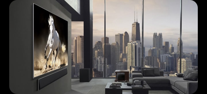 Luksusowy apartament na poddaszu. Panoramę miasta widać przez okna od podłogi do sufitu. LG True Wireless TV i LG Soundbar wiszą na ścianie. Przestrzeń jest bardzo elegancka i uporządkowana. Zero Connect Box jest ledwo widoczny pod jednym ze stolików.