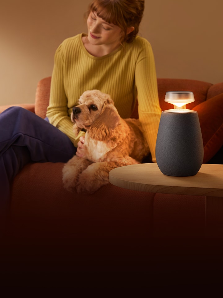 Uma mulher está a relaxar com o LG XBOOM XO2T e o seu cão no sofá.