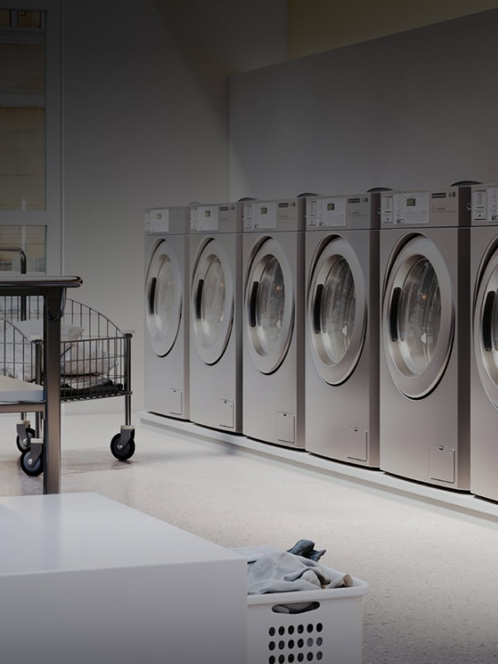 Row of LG commercial washing machines and dryers in a professional laundry facility, text overlay LG commercial laundry solutions