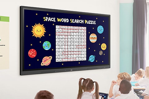 Suasana kelas dengan anak-anak duduk di kursi sambil menyaksikan layar besar yang menampilkan 'Teka-Teki Pencarian Kata Bertema Luar Angkasa' dengan planet dan bintang di sekitar kisi teka-teki.
