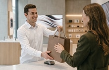 A smiling customer receives a shopping bag from a female shop assistant across the counter in a boutique.