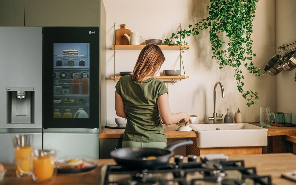 Una mujer en la cocina con un frigorífico transparente