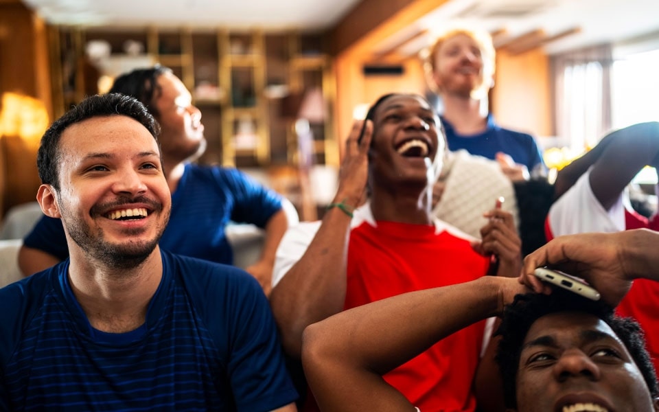Un grupo de hombres mira alegremente un partido de fútbol en un televisor calibrado, absortos en risas y sonrisas.