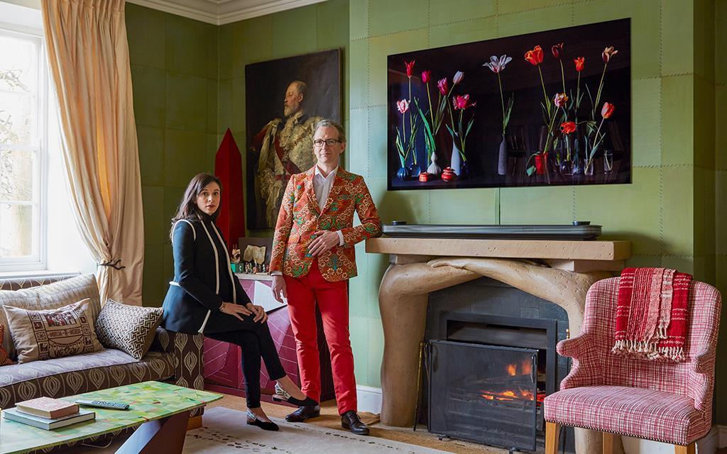 Ashley Hicks and his wife in their living room of their Oxfordshire home, with fireplace, antique chairs and numerous pieces of art