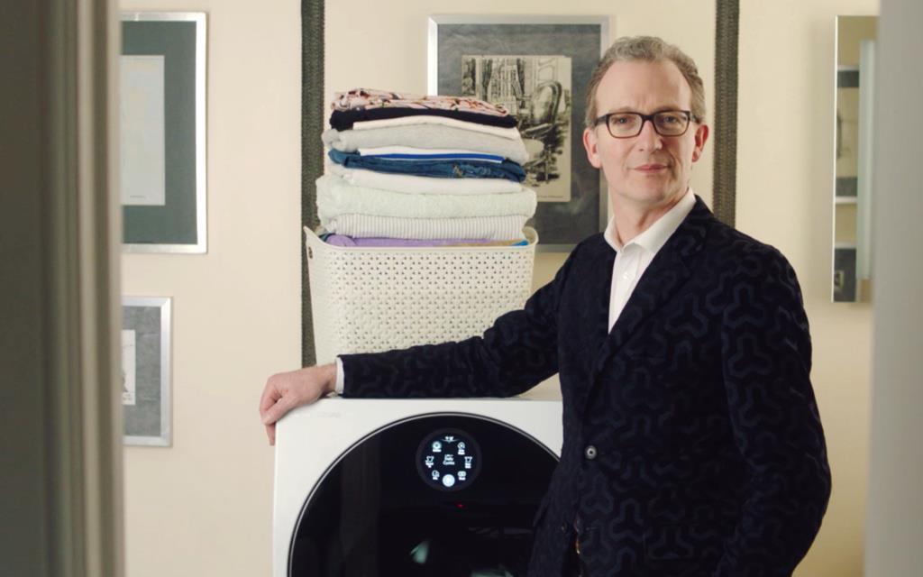Ashley Hicks with his hand on the LG SIGNATURE TWINWash washing machine with a pile of laundry in the background