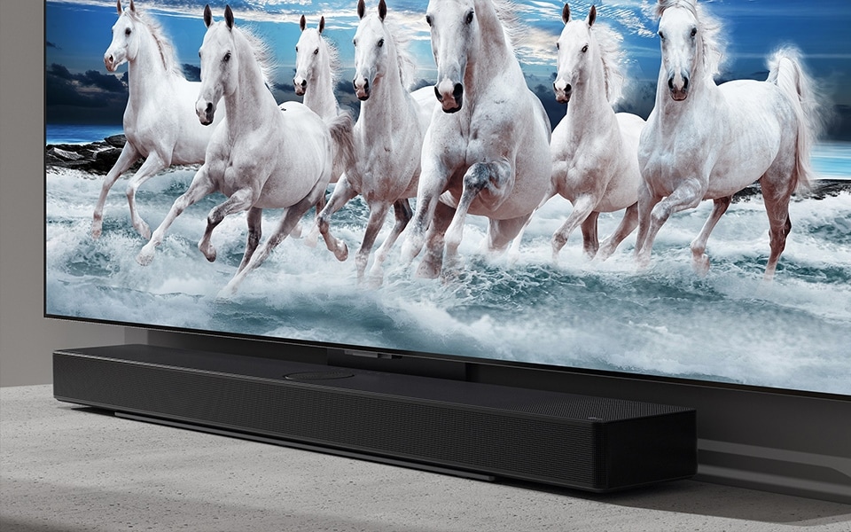 Una elegante barra de sonido Bluetooth combina a la perfección con un televisor LG con una imagen de caballos blancos.