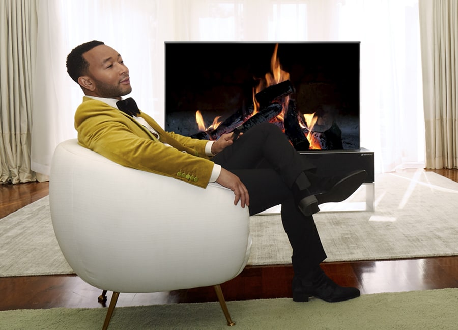 John Legend sentado en una silla blanca ante un televisor OLED enrollable LG SIGNATURE.