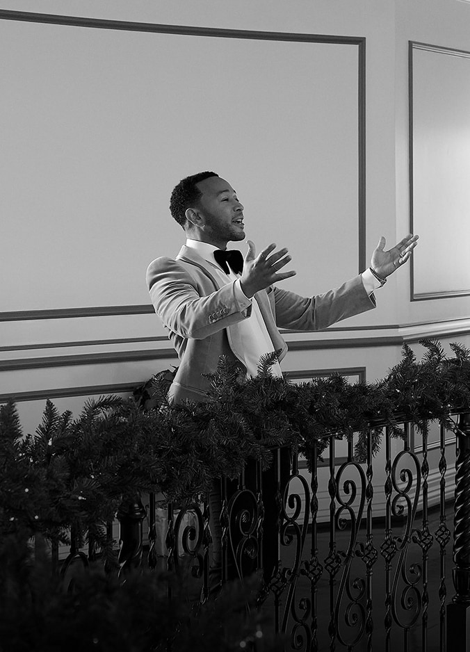 El cantante John Legend bajando una escalera agarrándose a un pasamanos decorado con decoración navideña.