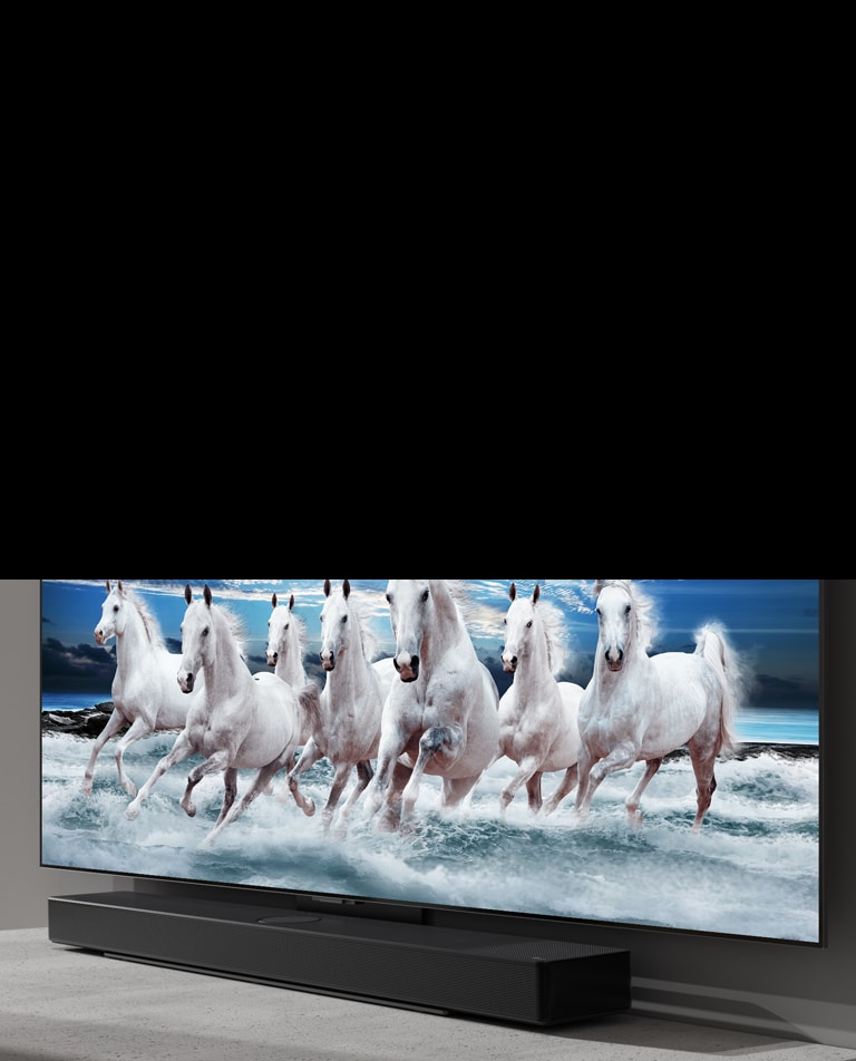 На белом столе расположены саундбар и телевизор, а на экране телевизора показано 7 белых лошадей.