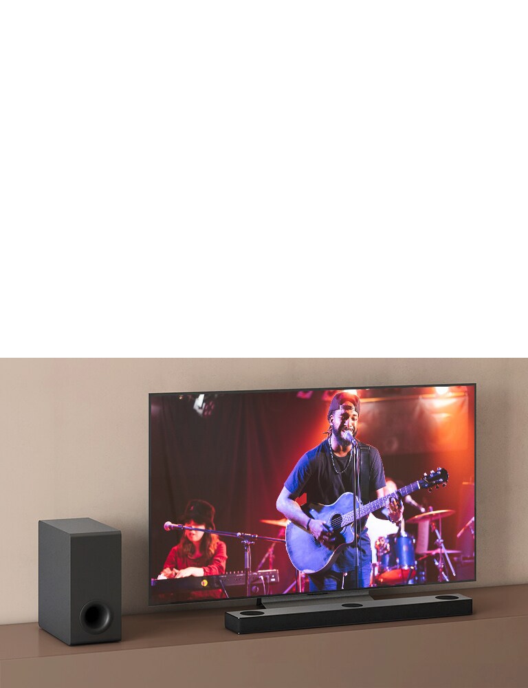 На экране телевизора LG концерт, а саундбар LG расположен под телевизором. Слева сабвуфер на коричневой полке.