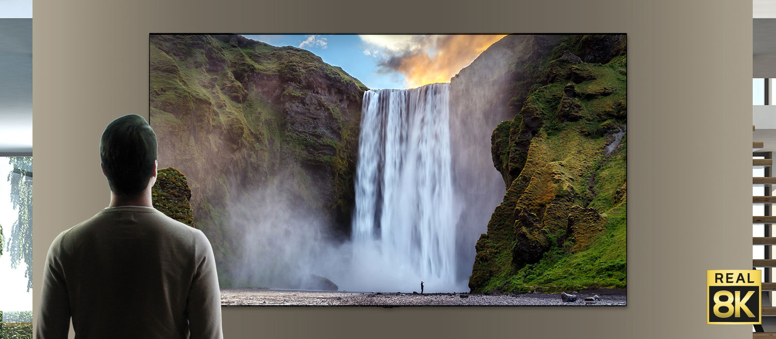 Человек, стоящий перед великолепным водопадом, обрушивающимся с горы. Камера отъезжает, и зрителю становится видно, что это изображение на телевизоре, закрепленном на стене.