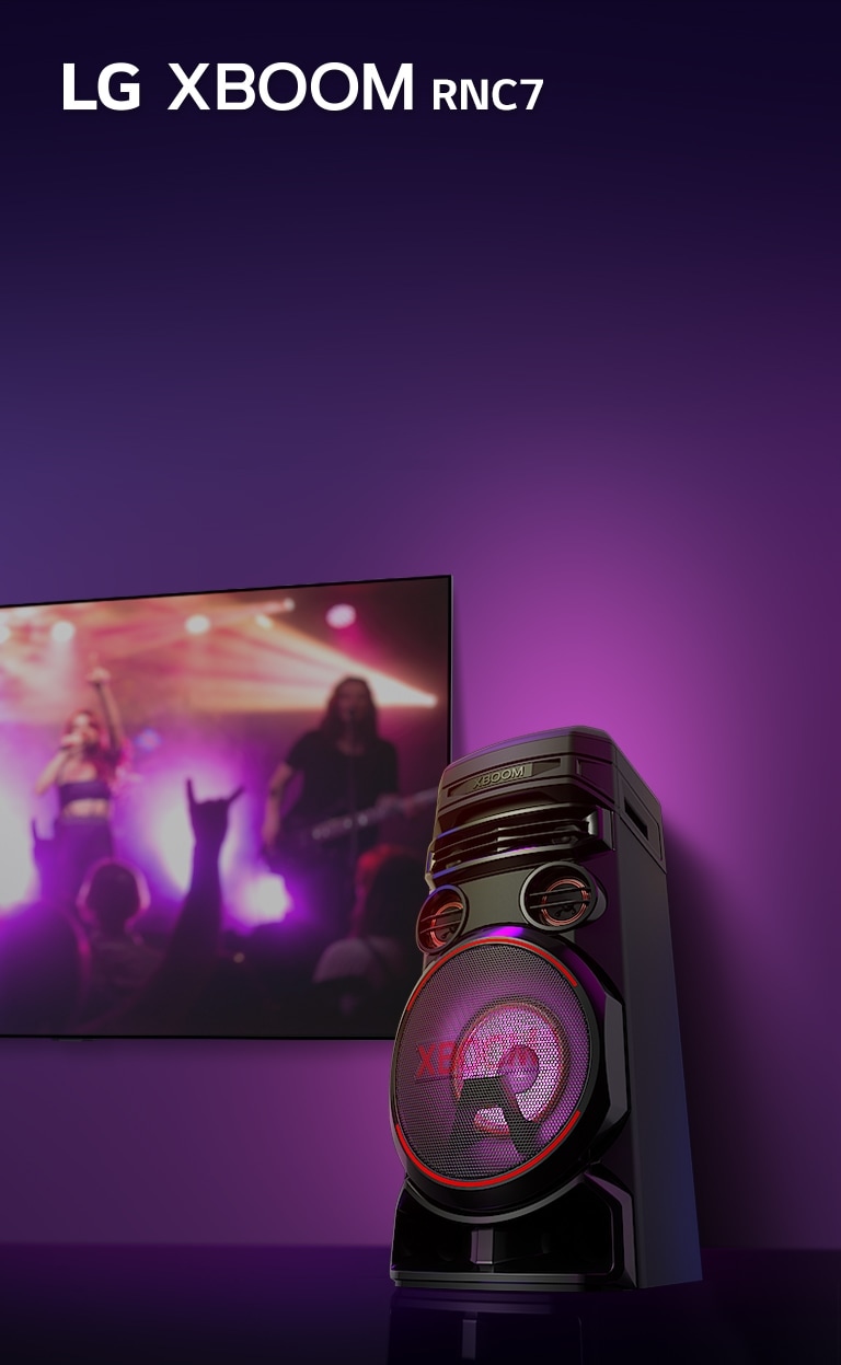 A low angle view of the right side of LG XBOOM rnc7 against a purple background.  The XBOOM light are also purple. And a TV screen displays a concert scene.