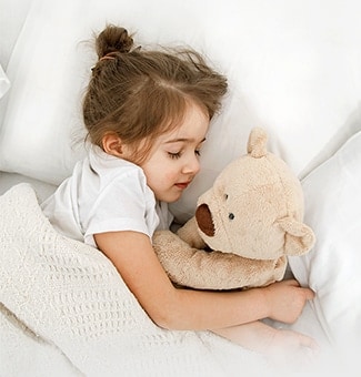 A little girl is lying in bed with a doll in her arms