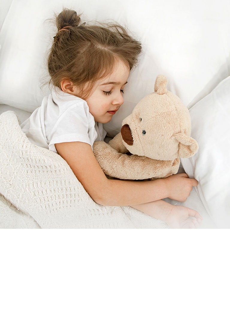 A little girl is lying in bed with a doll in her arms