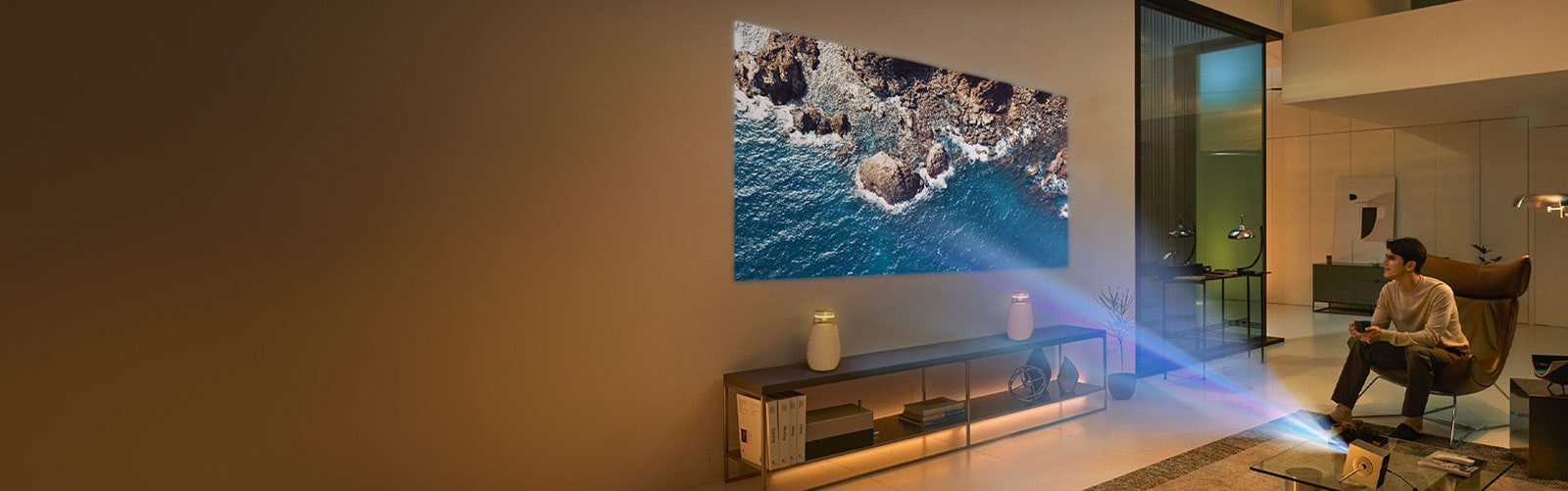 A man sitting on the sofa enjoying a 4K video on a large screen projected on the living room wall with the CineBeam Q HU710PB and XBOOM speaker.	