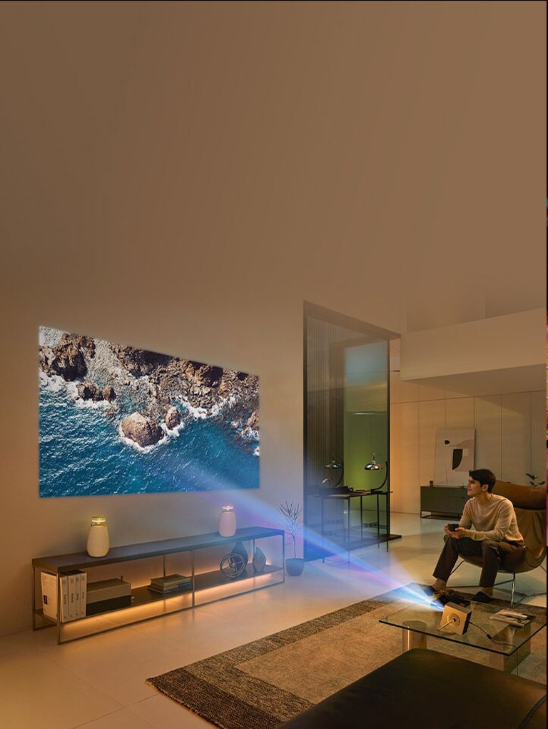 A man sitting on the sofa enjoying a 4K video on a large screen projected on the living room wall with the CineBeam Q HU710PB and XBOOM speaker.	