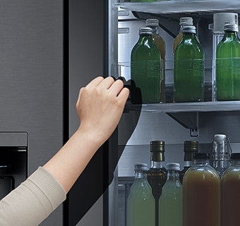 The front view of a black glass InstaView refrigerator with the light on inside. Hands tapping on InstaView screen.