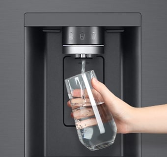 A person is getting water from the refrigerator dispenser in a cup