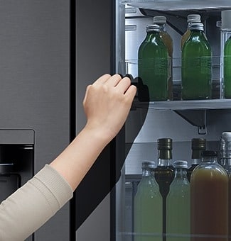 The front view of a black glass InstaView refrigerator with the light on inside. Hands tapping on InstaView screen.