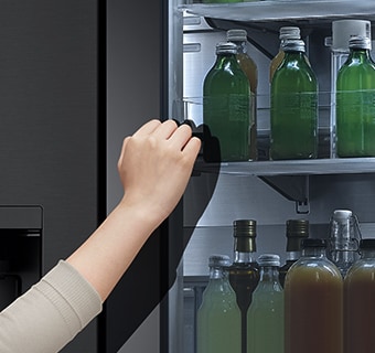 The front view of a black glass InstaView refrigerator with the light on inside. Hands tapping on InstaView screen.