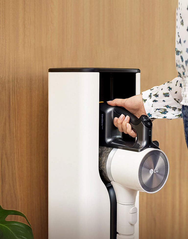 A woman is putting in a Cordzero™ Vacuum cleaner in a docking station.