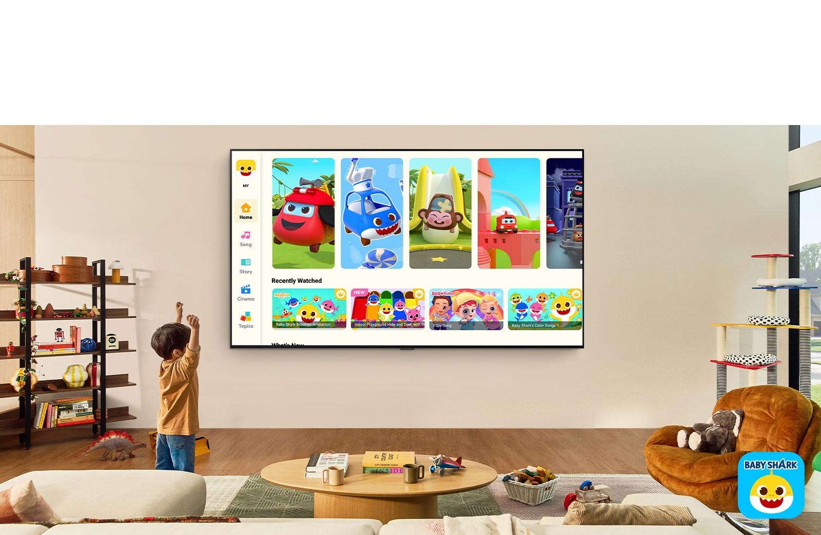 صبي صغير يشاهد Pinkfong على تلفزيون LG TV مثبت على الحائط في غرفة معيشة مع وجود ألعاب أطفال. 