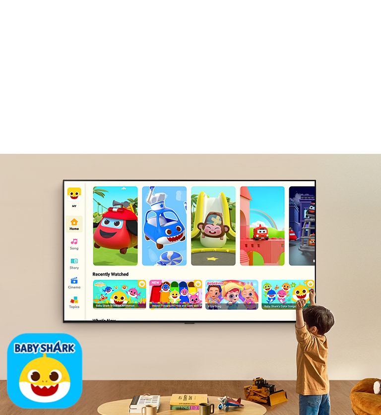 صبي صغير يشاهد Pinkfong على تلفزيون LG TV مثبت على الحائط في غرفة معيشة مع وجود ألعاب أطفال. 