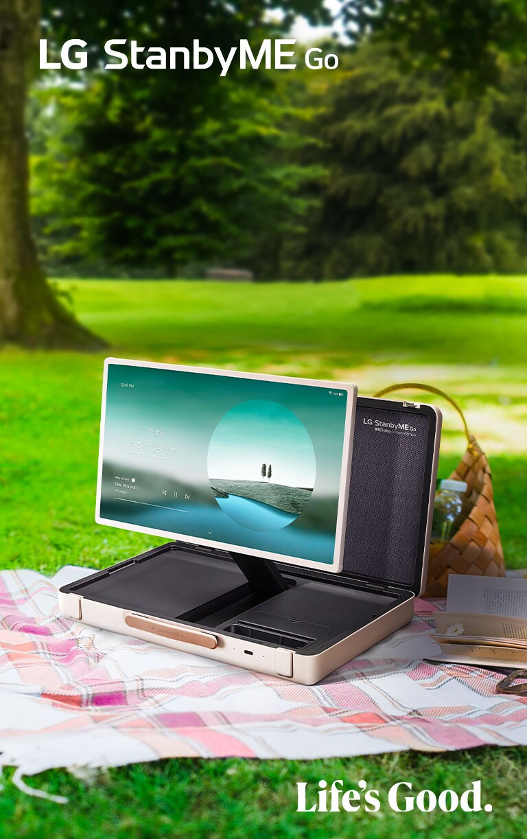 LG StanbyME Go is placed on a checkered picnic blanket with left side forward, displaying a weather themed home screen.