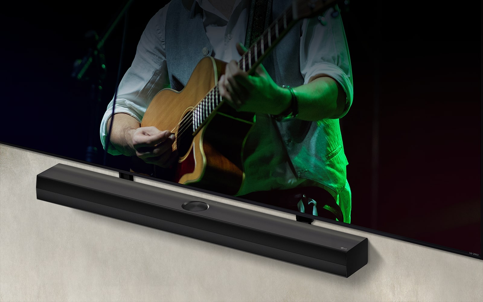 LG Soundbar against a black backdrop reveals its design starting from the left corner, then pans out to show the whole soundbar. An LG QNED TV appears with Synergy Bracket. The Soundbar sits on top of the Synergy Bracket, presses against the wall with the lower screen of the TV being visible, displaying a man playing the guitar.