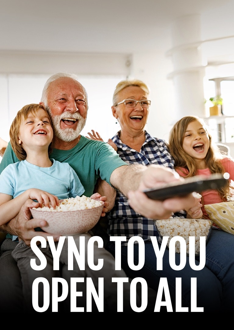 A family sits laughing while the grandfather points the remote outward. 