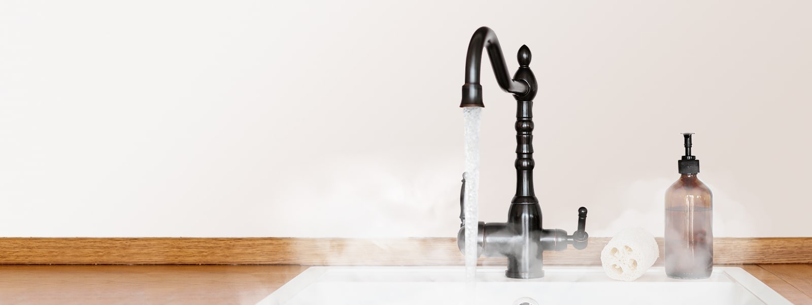 Steamy hot water pours from a black faucet into a white sink below, with a scrub and brown soap dispenser waiting at the faucet's right side.