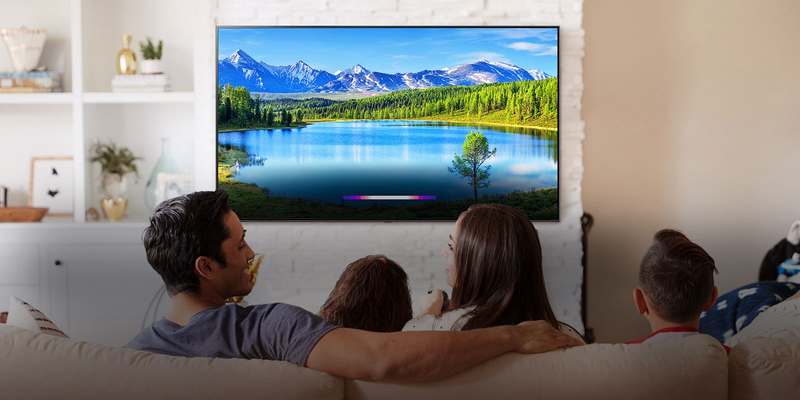 Family in bright living room looking at landscape on wall-mounted TV