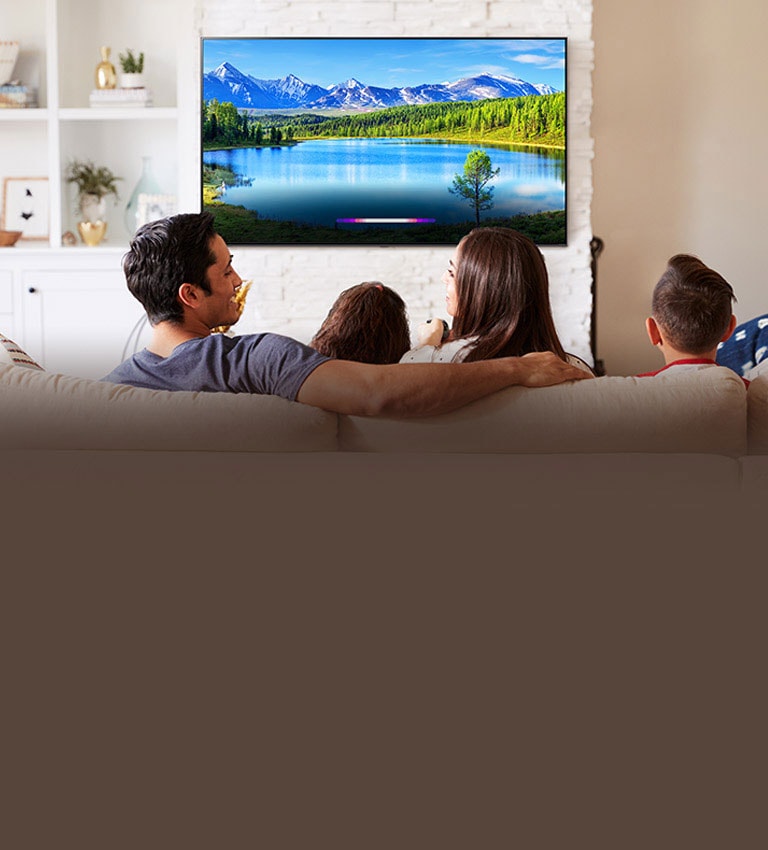 Family in bright living room looking at landscape on wall-mounted TV