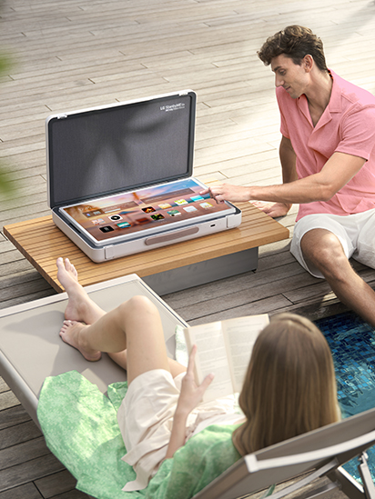 Le StanbyME Go est placé sur la table du patio, et l’écran est réglé en mode Table, affichant l’écran d’accueil. Un homme sur le point d’appuyer sur l’une des applications, tandis qu’une femme se détend.