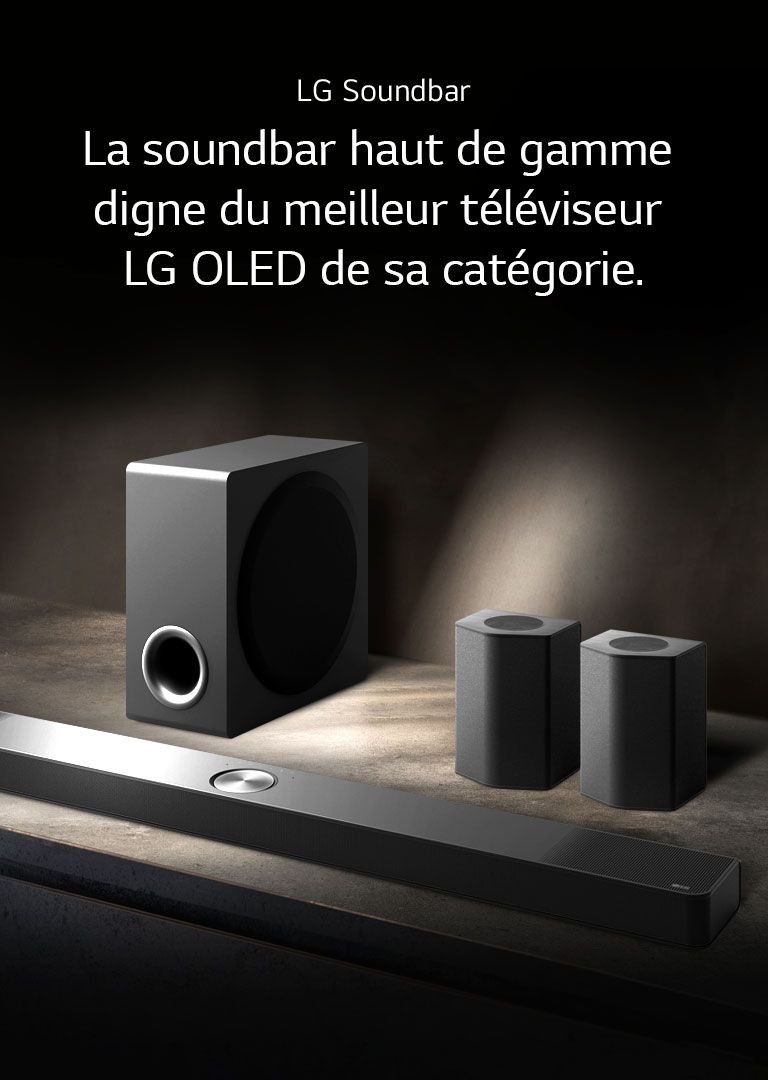 La LG Soundbar, les enceintes arrière et le caisson de basse installés en biais sur une étagère en bois marron dans une pièce obscure, avec une lumière qui n’éclaire que le système audio.