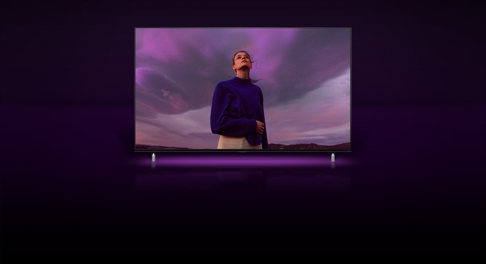 Una mujer está para mirando el cielo morado y la imagen se aleja y muestra a la misma mujer en la pantalla del televisor QNED TV.