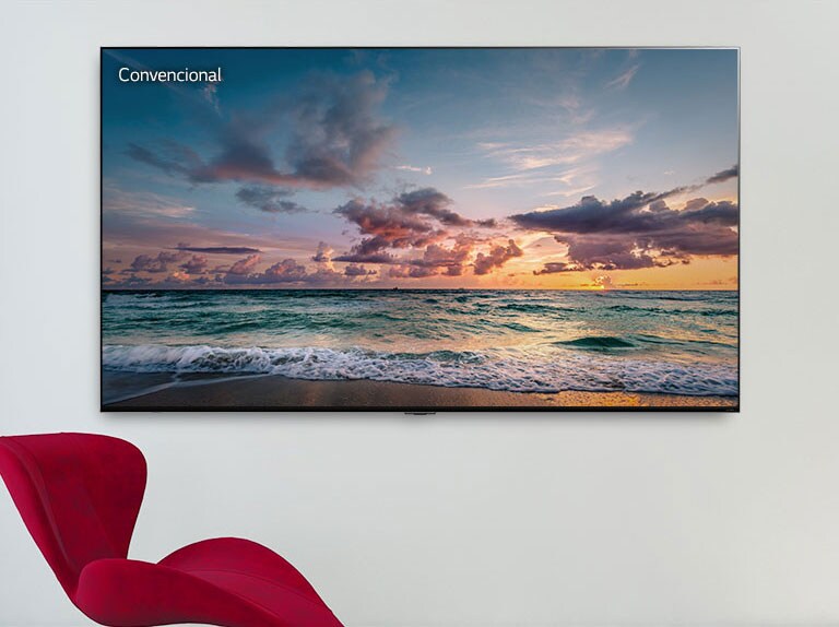 Un televisor de pantalla grande montado en una pared con una silla roja adelante. La pantalla muestra olas que rompen suavemente en una playa. Al desplazarse de izquierda a derecha se muestra la diferencia de color entre un televisor LCD convencional y un LG QNED Mini LED.