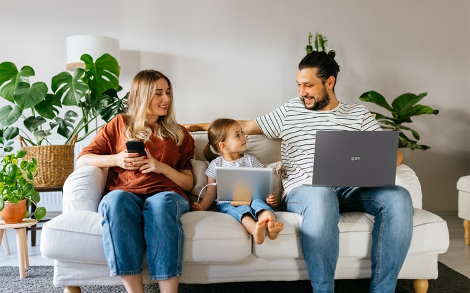 Familie auf dem Sofa mit Vater, der einen LG Gram-Laptop benutzt