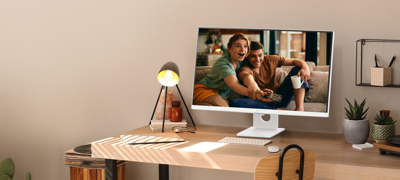 On the desk by the sunlit window, there is a smart monitor displaying a movie on its screen. Beside the monitor, there is a lamp and a potted plant. On the desk, there is a keyboard and a mouse.
