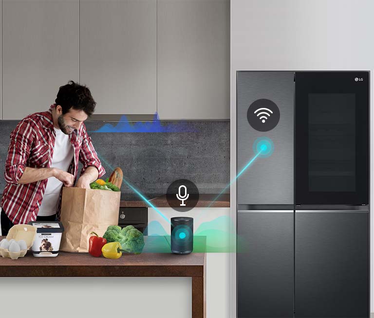 A man stands in a kitchen unloading produce from a grocery bag and speaks, shown by volume bars moving up and down near him, to the AI speaker on the counter telling it to 