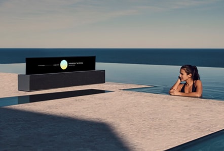 A woman in a pool listens to a Rollable OLED TV R in Line view.