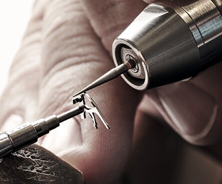 A close-up shot on the fingers of a craftsperson shows them working with a watch component.